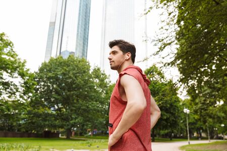 Photo of serious man wearing sportswear listening music with earphones while working out in city parkの写真素材