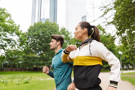 Photo of sporty serious man and woman wearing sportswear doing workout and running in city park