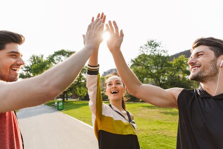 Photo of excited joyful people wearing sportswear standing with raising arms together while working out in city parkの写真素材