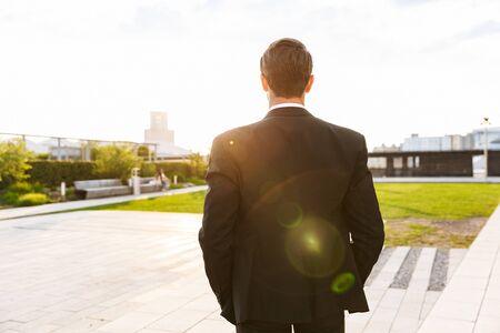 Back view of a young businessman wearing suit standing outdoors at the city streetsの写真素材