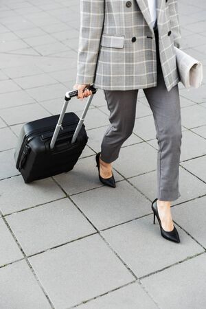 Cropped image of a businesswoman wearing suit outdoors at the downtown, carrying suitcaseの写真素材