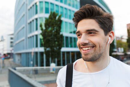 Handsome smiling young man dressed casually spending time outdoors at the city, listening to music with earphonesの写真素材