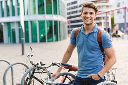 Handsome smiling young man dressed casually spending time outdoors at the city, carrying backpackの写真素材