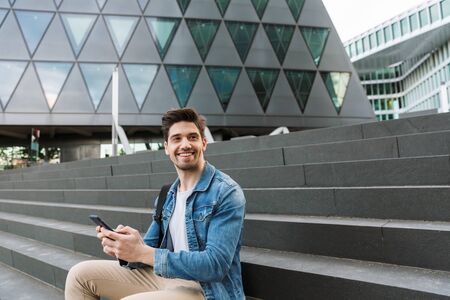 Handsome young man dressed casually spending time outdoors at the city, sitting on stairsの写真素材