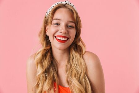 Image of positive young woman with long curly hair smiling and looking at camera isolated over pink backgroundの写真素材