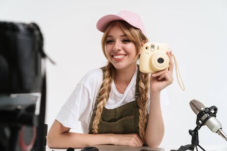 Image of hipster girl recording blog broadcast with microphone about new photocamera isolated over white wall in studioの写真素材