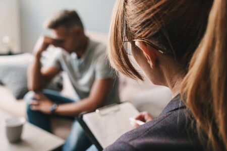 Photo of upset handsome man having conversation with psychologist on therapy session in room