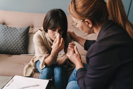 Photo of depressed caucasian woman crying and having conversation with psychologist on therapy session in roomの写真素材
