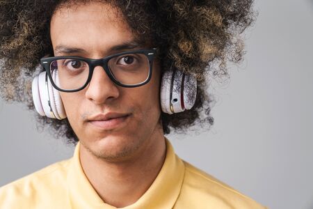Photo of handsome caucasian man with afro hairstyle looking at camera while wearing headphones and eyeglasses isolated over gray backgroundの写真素材