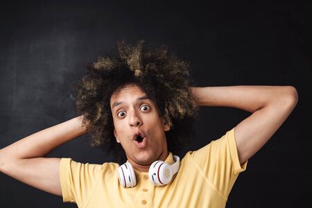 Photo of a curly young shocked emotional teenage guy posing over grey chalkboard wall with...