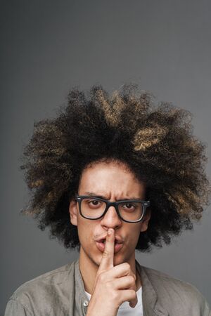 Image of a young curly serious teenage guy posing isolated over grey wall background showing silence gesture.の写真素材