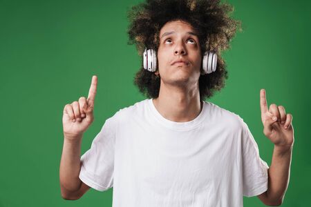 Photo of a young concentrated curly guy posing isolated over green wall background listening music...