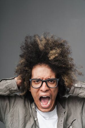 Photo closeup of stressed young man with afro hairstyle grabbing his head and shouting and isolated...
