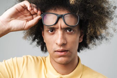 Photo of puzzled caucasian man with afro hairstyle wearing eyeglasses frowning at camera isolated...