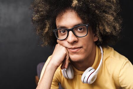 Photo of a curly young pleased teenage guy posing over grey chalkboard wall with headphones.の写真素材