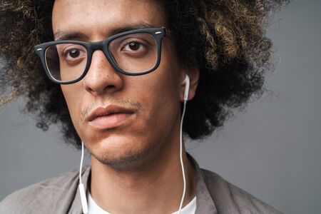 Photo closeup of thinking brunette man with afro hairstyle looking aside and using earphones isolated over gray backgroundの写真素材