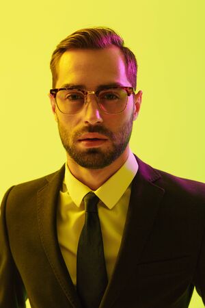 Image of a handsome young serious business man posing isolated over light green background wall with led neon lights.の写真素材