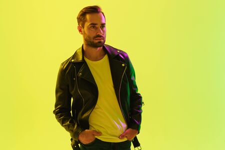 Picture of attractive handsome young stylish man posing isolated over light green background wall with led neon lights dressed in leather jacket.の写真素材