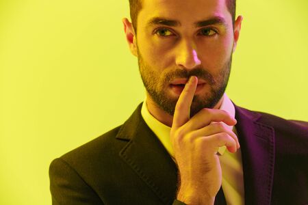 Image of puzzled young businessman in formal suit holding hand at his mouth isolated over yellow backgroundの写真素材