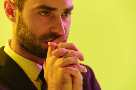 Image of serious young businessman in formal suit holding hands at his mouth isolated over yellow backgroundの写真素材