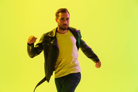 Attractive young man wearing leather jacket jumping isolated over yellow backgroundの写真素材