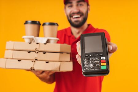 Portrait of caucasian delivery man in red uniform holding pizza boxes and payment terminal isolated...