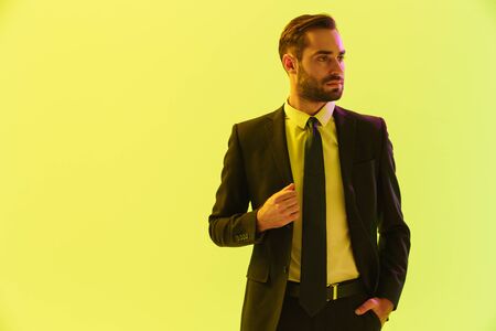Image of masculine serious businessman in formal suit touching his jacket isolated over yellow backgroundの写真素材