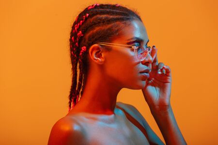 Portrait of beautiful young african naked woman posing isolated over yellow neon lights wall...