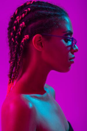 Picture of serious beautiful young african naked woman posing isolated over purple neon lights wall background wearing sunglasses.の写真素材