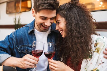 Portrait of laughing couple man and woman drinking red wine while hugging together near trailer outdoorsの写真素材