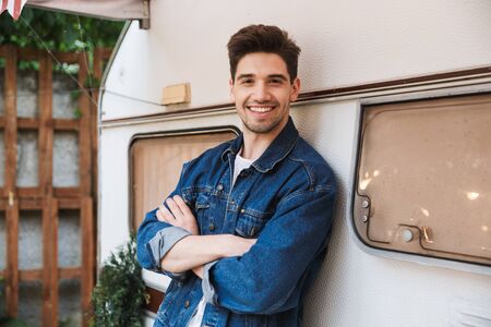Portrait of happy handsome man wearing denim jacket smiling and looking at camera while standing...