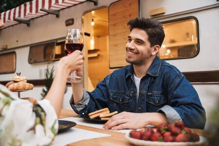 Portrait of happy couple man and woman drinking red wine while eating sandwiches together at wooden table outdoorsの写真素材