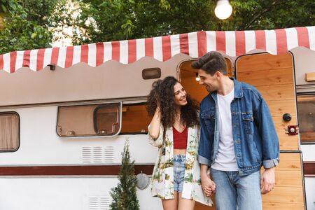 Cheerful young couple talking while standing at the campvan, holding hands
