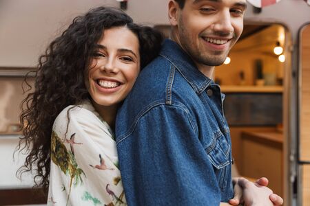 Portrait closeup of romantic couple man and woman smiling while hugging together near house on wheels outdoorsの写真素材