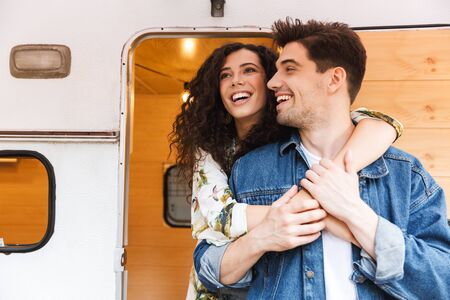 Cheerful young couple talking while standing at the campvan, hugging