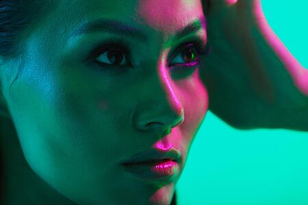 Beauty close up portrait of an attractive topless young asian woman with long wet hair standing isolated over blue neon background, posingの写真素材