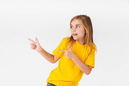 Portrait of little blonde summer girl wearing casual t-shirt looking aside and pointing fingers at copyspace isolated over white backgroundの写真素材