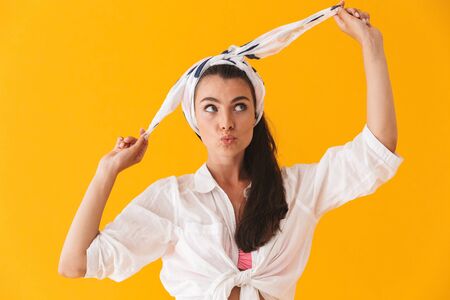 Beautiful lovely young girl wearing summer clothes standing isolated over yellow background, posing, looking awayの写真素材