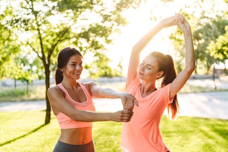 Image of beautiful fitness women in sportswear smiling and doing workout at green park in morningの写真素材