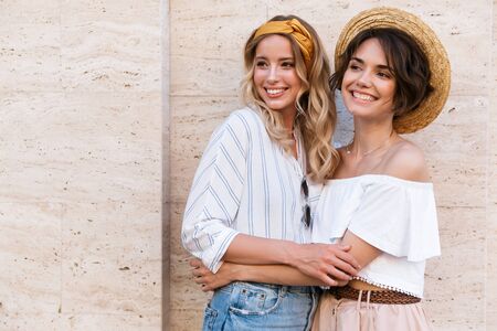 Image of a cheery pleased positive young girls friends posing outdoors hugging looking aside.の写真素材
