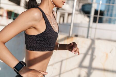 Cropped image of young strong sports woman outdoors at the beach at morning running listening music.