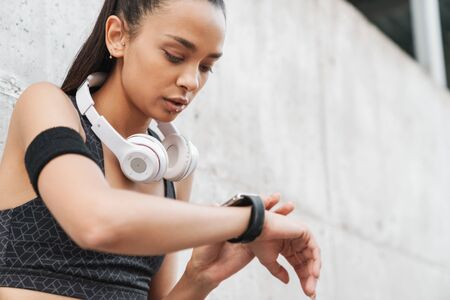 Close up of an attractive young fitness girl leaning on a wall while standing outdoors, resting...