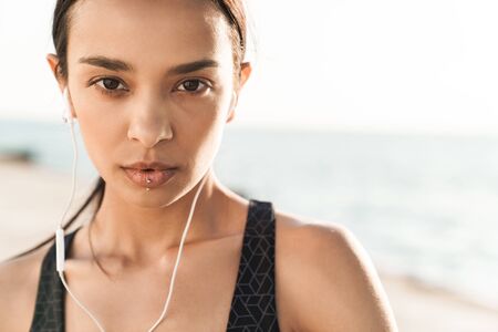 Image of a pretty beautiful serious strong sports woman outdoors at the beach at morning listening...
