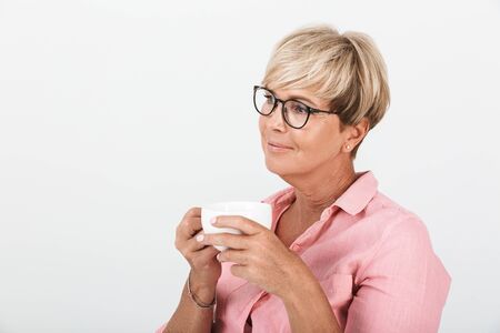Portrait of gorgeous middle-aged woman wearing eyeglasses smiling and holding coffee cup isolated over white backgroundの写真素材