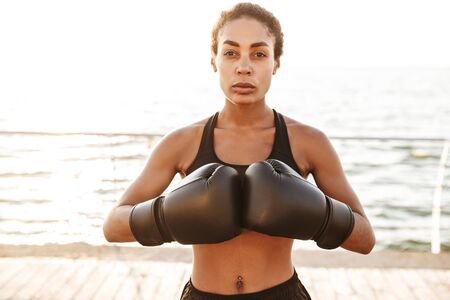 Image of attractive pretty woman wearing sportive clothes training in boxing gloves by seaside in...