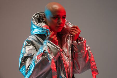 Portrait of an attractive bald woman wearing warm jacket standing isolated over gray background...