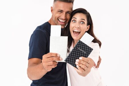 Cheerful attractive couple wearing casual outfit standing isolated over white background, showing passports with flight ticketsの写真素材
