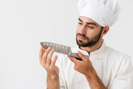 Image of serious chief man in cook uniform holding big sharp metal knife isolated over white wall