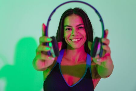 Image of beautiful smiling optimistic young strong fitness woman isolated with led flash lights give you a headphones.の写真素材