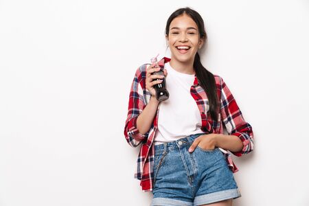 Image of a cheery happy young pretty teenage girl posing isolated over white wall background with...